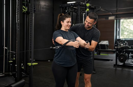 Coach guiding a member through a cable exercise on the gym floor